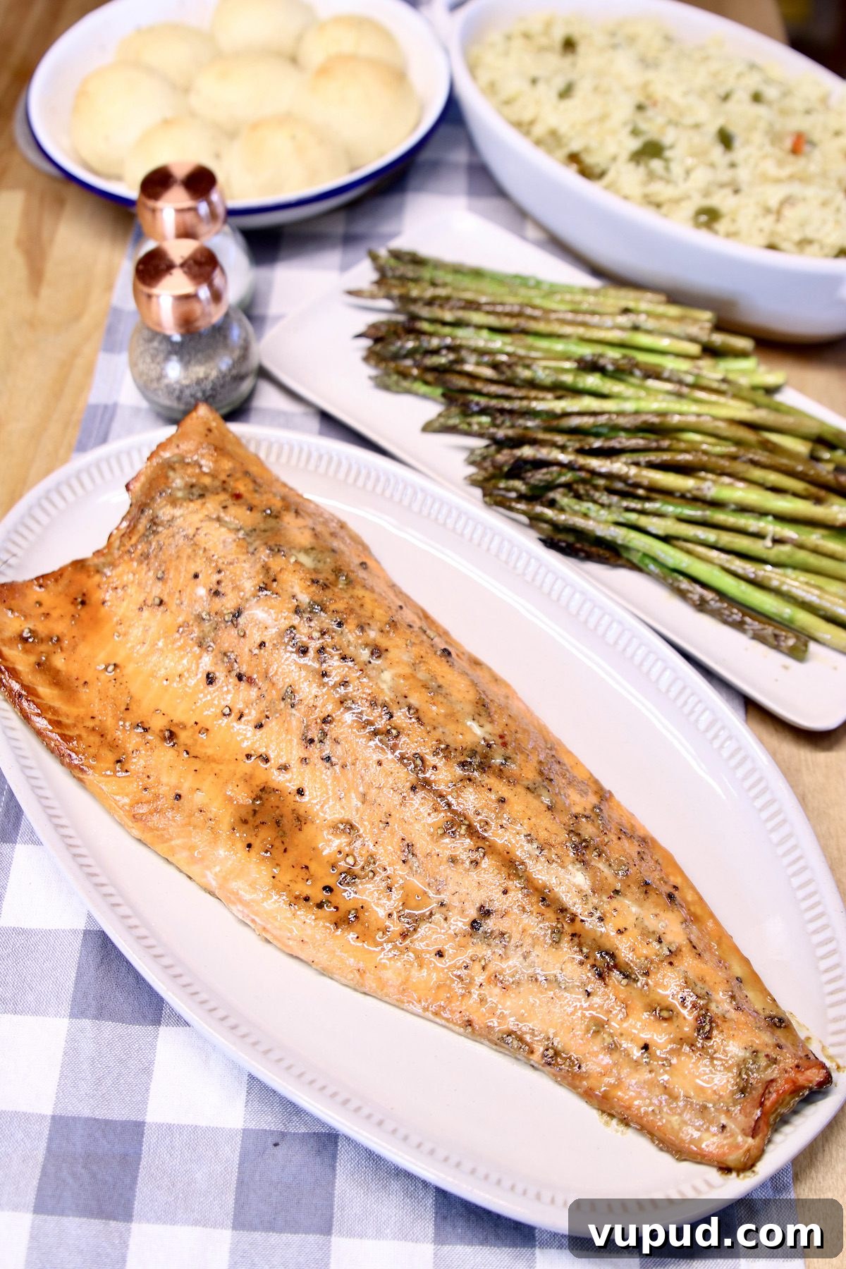 Grilled salmon filet with maple glaze for a quick and easy dinner grilled salmon filet on a platter, bowl of rice, asparagus, pan of dinner rolls in background.