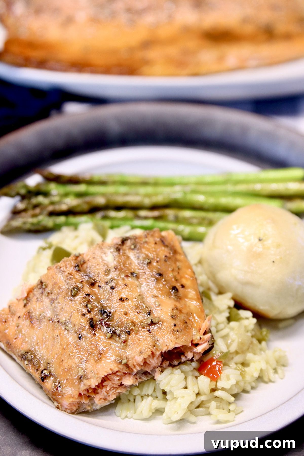 Maple Glazed Salmon is a delicious meal to make on the grill that is quick and easy. salmon filet over rice with roll and asparagus on a plate.