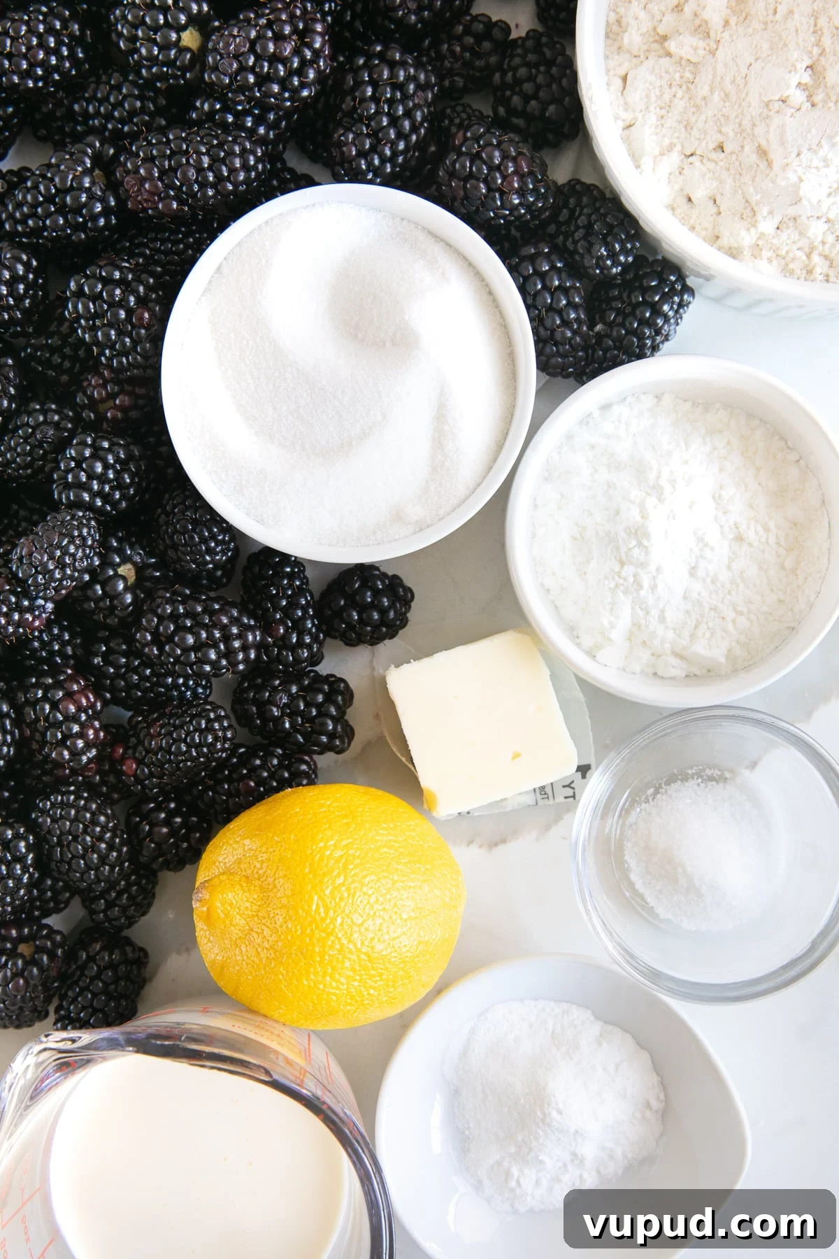 Classic Blackberry Cobbler Recipe: Sweet, Juicy, Homemade Dessert 3 All of the ingredients needed to make homemade blackberry cobbler measured and placed in individual small bowls or laid out on a white table.