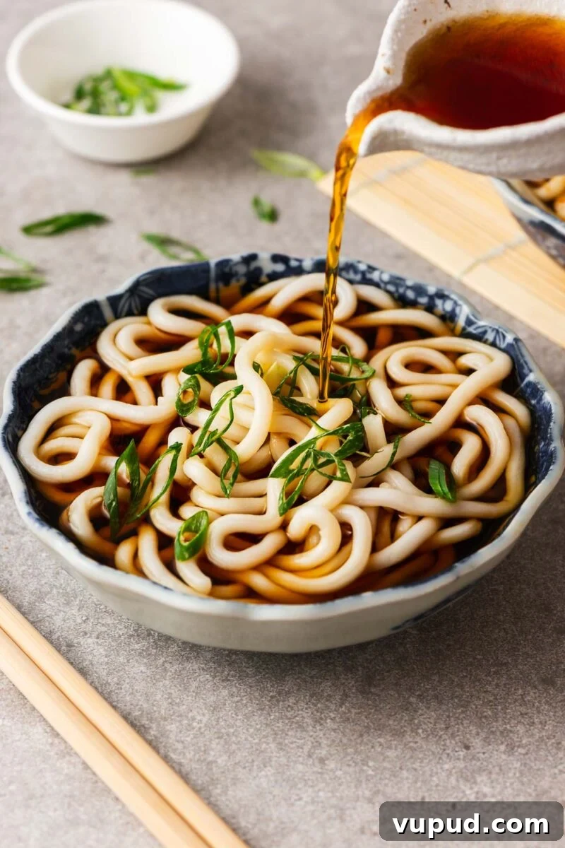 Authentic Thai Red Curry with Fish: Quick Flavorful Recipe 12 Pouring kake udon noodle broth over a Japanese bowl with udon noodles.