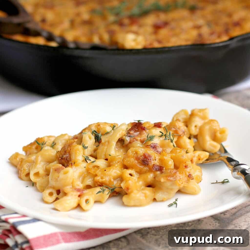 Garlic, Bacon & Beer Macaroni and Cheese Recipe 2 side view of finished bacon macaroni and cheese plated on a white dish; remainder of the mac n cheese is in the background in a cast iron skillet (zoomed view)