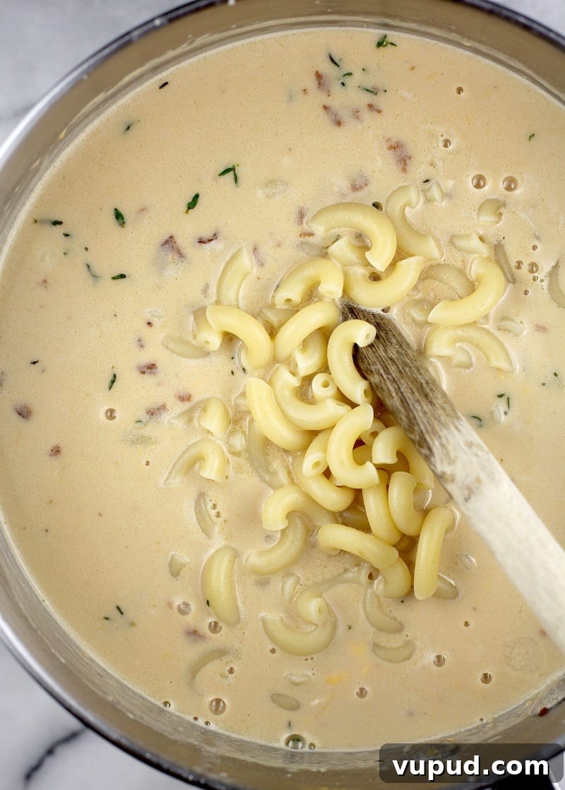 Garlic, Bacon & Beer Macaroni and Cheese Recipe 8 macaroni being added to the cheese sauce, top down view in a saucepan
