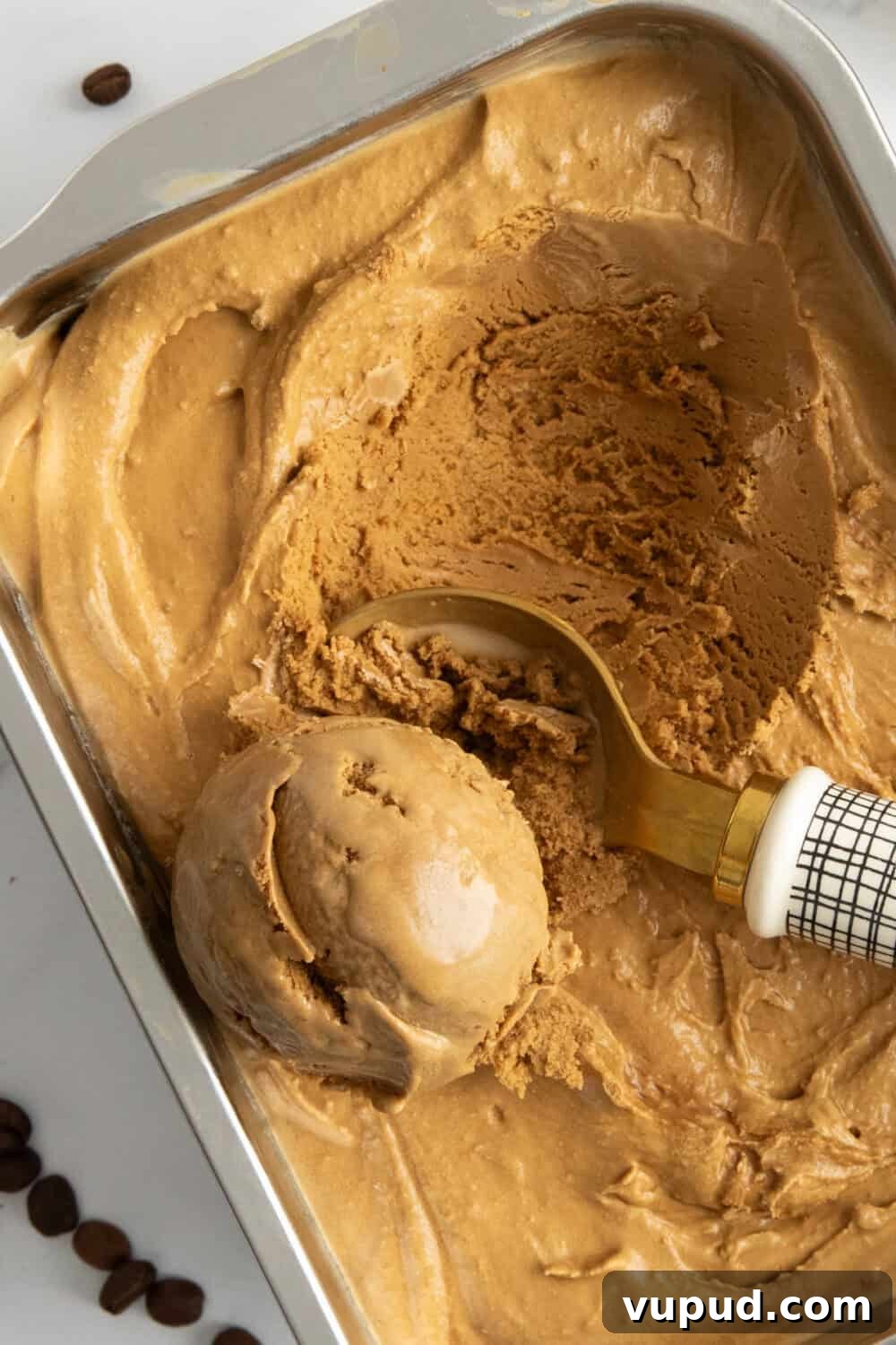Homemade Espresso Ice Cream Recipe: Rich Coffee Gelato at Home 2 A pan of espresso coffee ice cream being scooped by an ice cream scooper. Espresso beans are in the background.