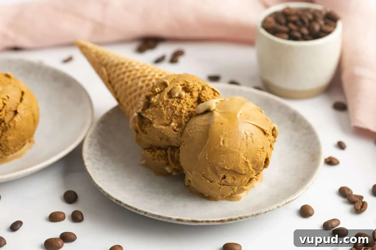 Homemade Espresso Ice Cream Recipe: Rich Coffee Gelato at Home 7 Homemade espresso ice cream in a cone laid on a plate. Espresso coffee beans are scattered around.