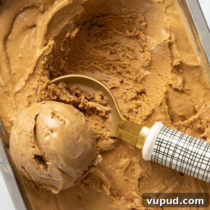 A pan of espresso coffee ice cream being scooped by an ice cream scooper. Espresso beans are in the background.
