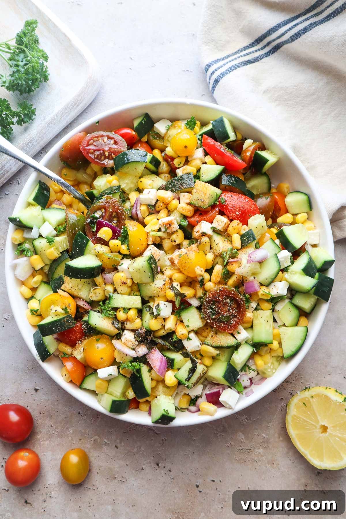 bowl with tomato corn cucumber salad tossed in lemon juice and olive oil.