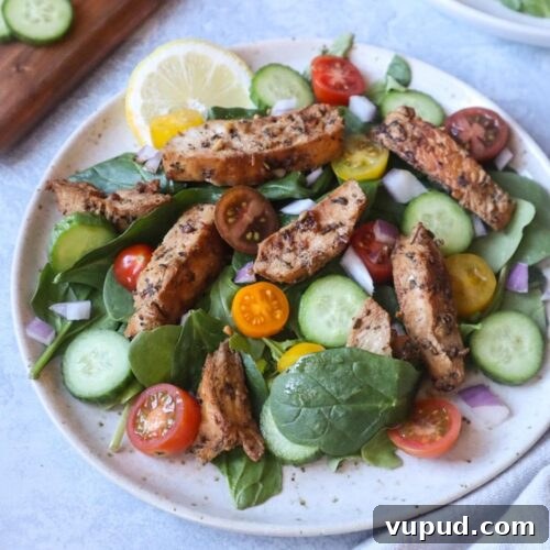 white plate with salad topped with tomatoes, cucumber, and cooked chicken