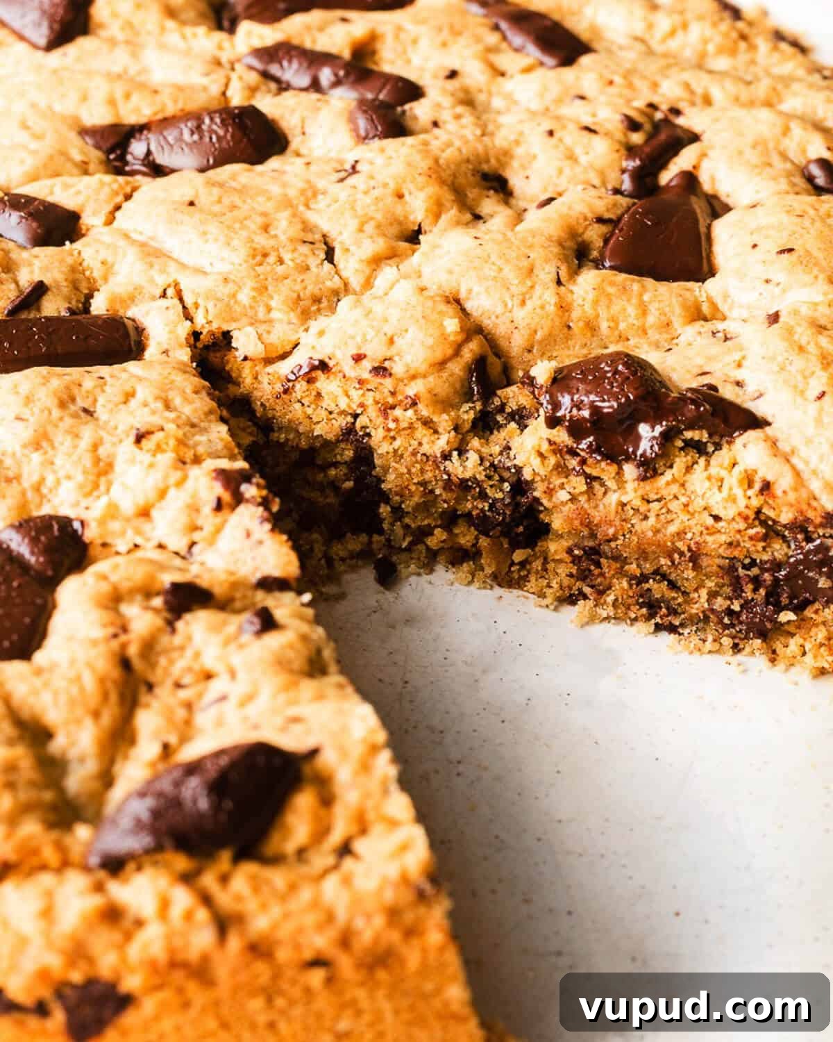 A Giant Choc Chip Cookie on a white plate, a slice is missing and you can see the gooey texture.