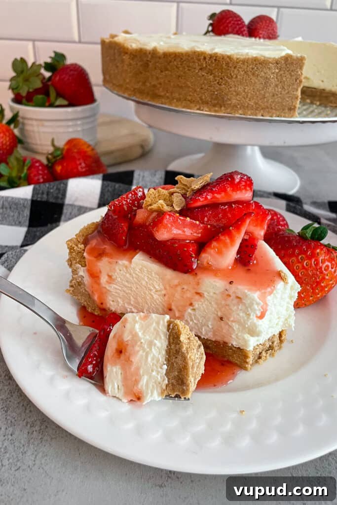 No-Bake Strawberry Cheesecake with Fresh Strawberries 4 a slice of strawberry cheesecake on a white serving plate topped with fresh strawberry syrup. A bite is taken out of it and shown on the fork next to the cheesecake