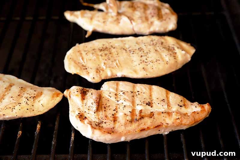 Horizontal image of four chicken breasts cooking on a grill.