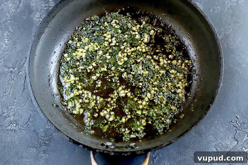 Horizontal overhead image of a nonstick saucepan filled about halfway with a lemon and herb sauce, on a gray surface.