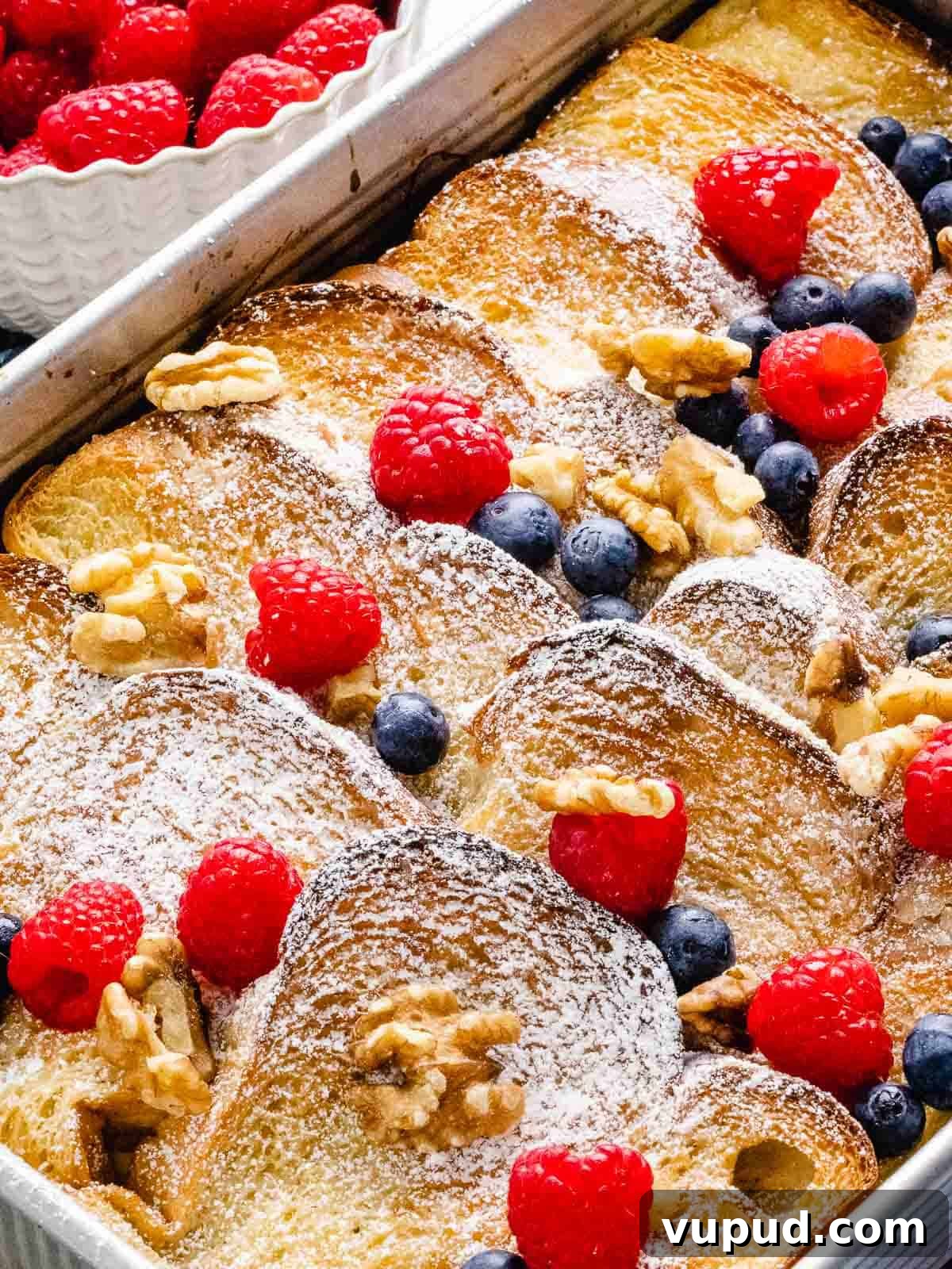 Make-Ahead Baked French Toast Casserole Recipe 2 Overhead of french toast casserole in a baking pan topped with blueberries, raspberries, and walnuts dusted with powdered sugar.