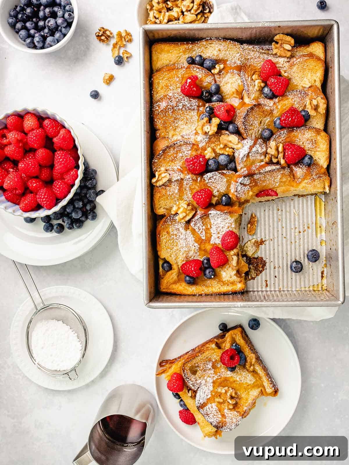 Make-Ahead Baked French Toast Casserole Recipe 9 Baked french toast in a baking pan with golden brown crispy crust topped with blueberries, raspberries, nuts, and maple syrup.