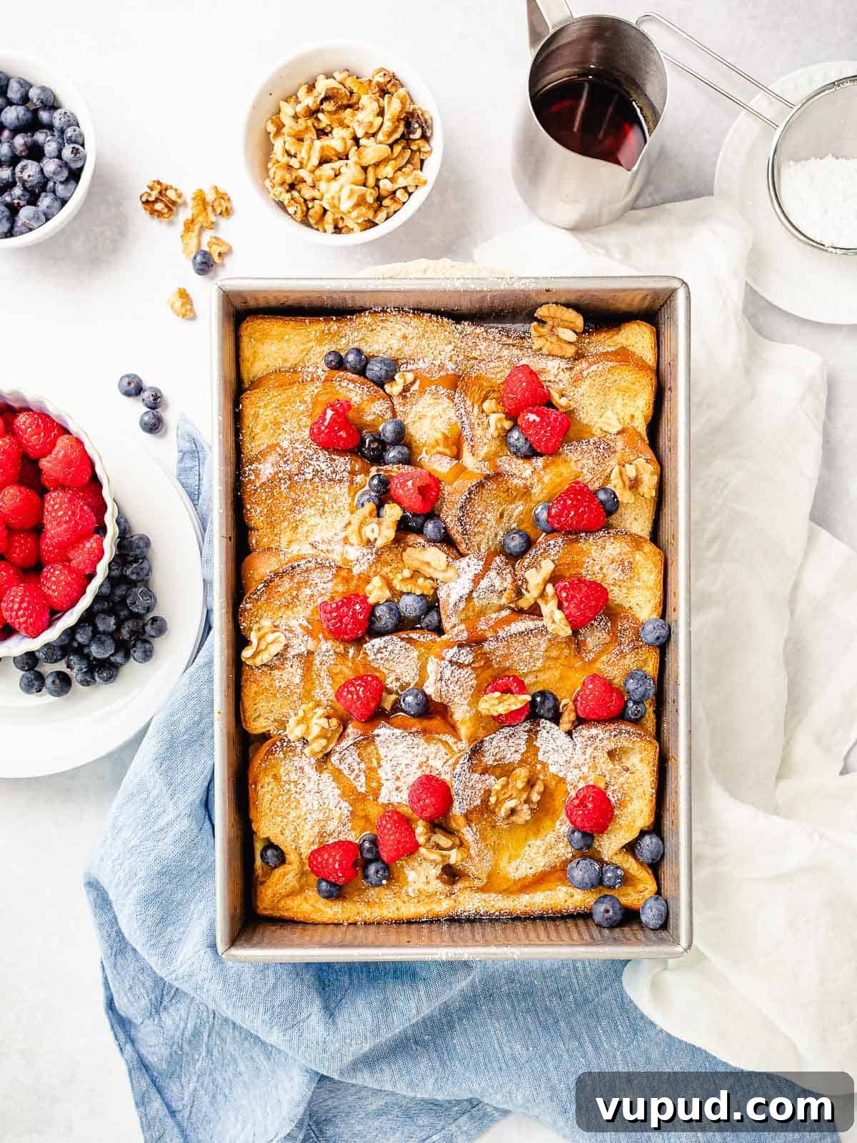 Make-Ahead Baked French Toast Casserole Recipe 3 Overnight baked french toast casserole with blueberries, rapsberries, and maple syrup surrounded by toppings.
