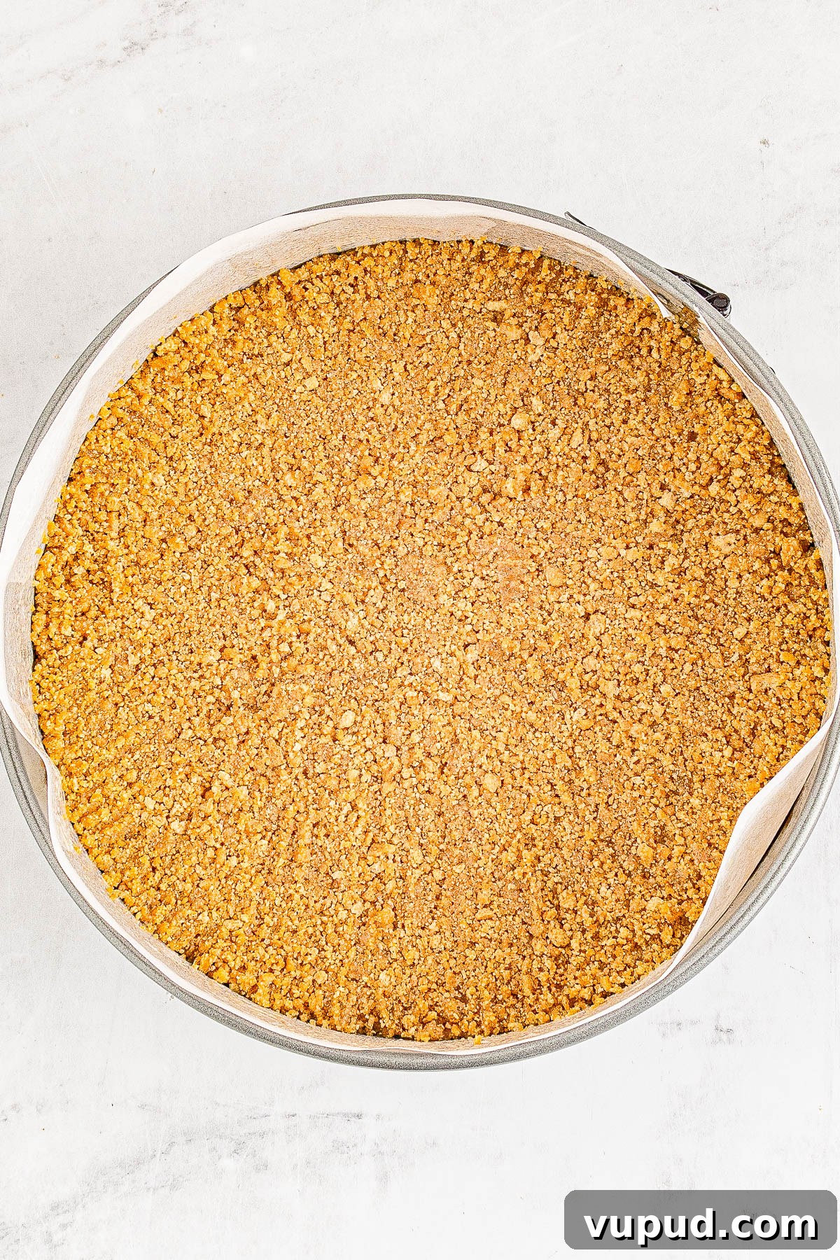 Classic New York Cheesecake Recipe: Creamy Oven-Baked Slice 11 A baked crumb crust in a round metal pan.
