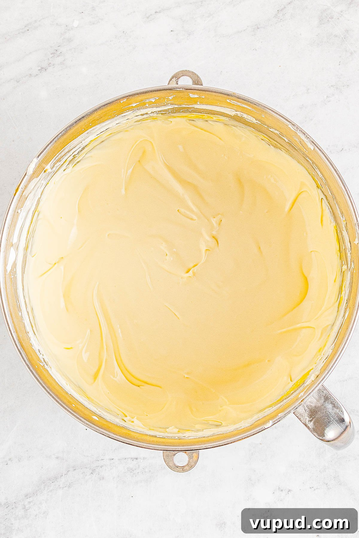 Classic New York Cheesecake Recipe: Creamy Oven-Baked Slice 15 A top-down view of a creamy batter in a mixing bowl on a marble surface.