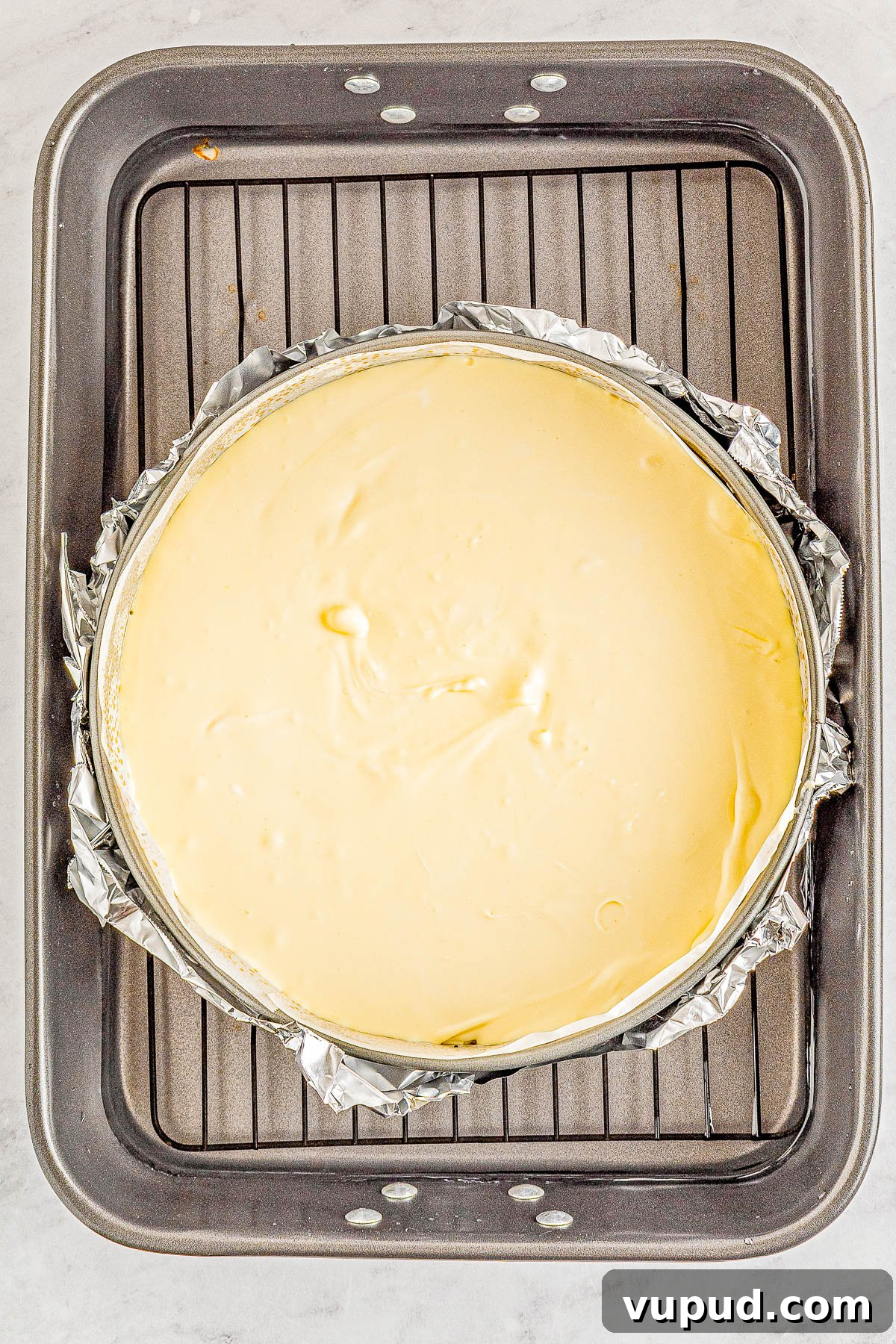 Classic New York Cheesecake Recipe: Creamy Oven-Baked Slice 17 A freshly baked cheesecake in a springform pan wrapped with foil on a cooling rack.