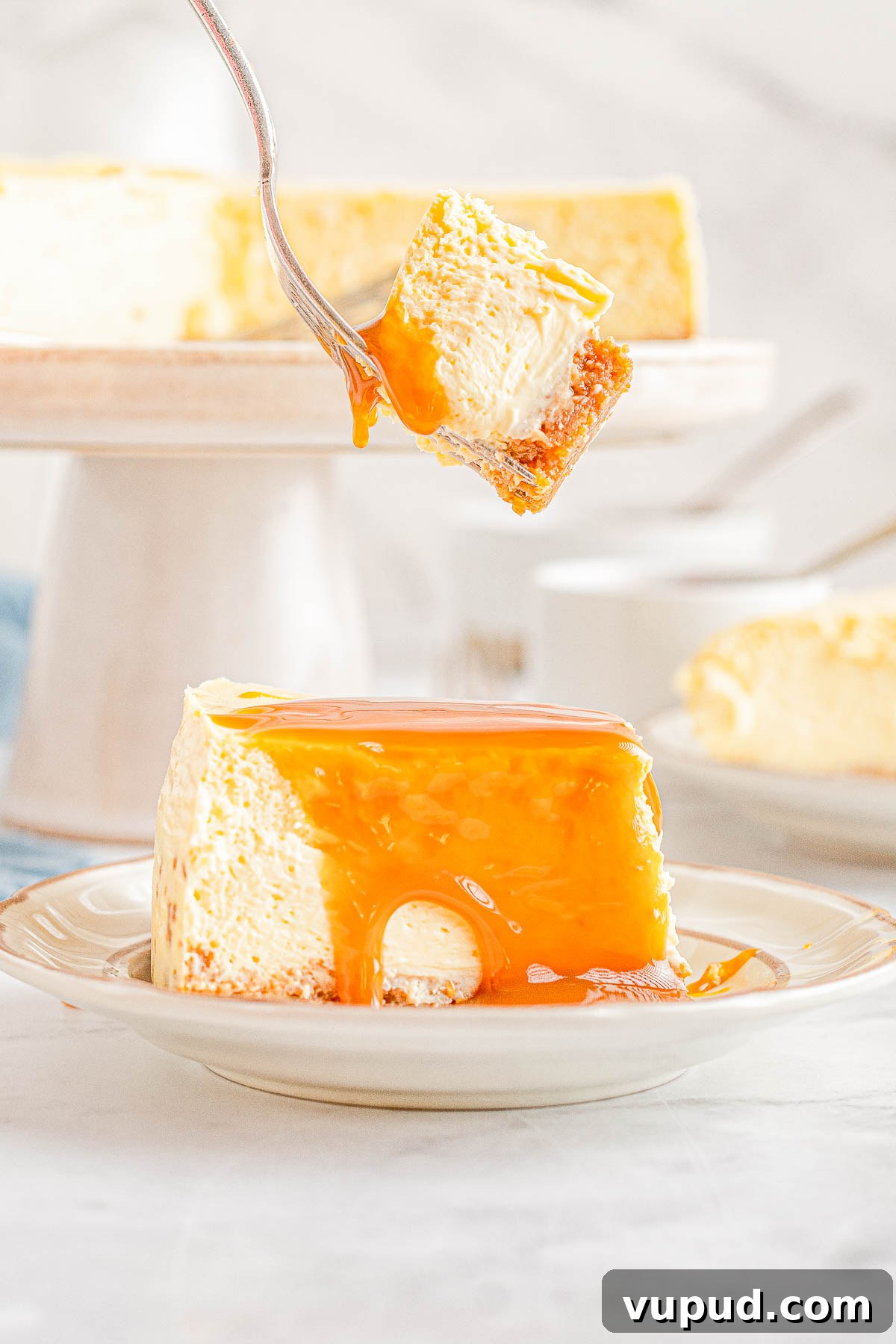 Classic New York Cheesecake Recipe: Creamy Oven-Baked Slice 23 A fork holding a bite of caramel-topped New York cheesecake over a plate with the rest of the slice of cake.