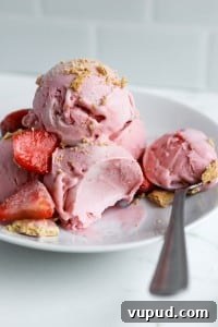 Strawberry Cheesecake Protein Ice Cream Recipe (Ninja Creami) 6 close up shot of strawberry ice cream with fresh strawberries in white bowl with silver spoon